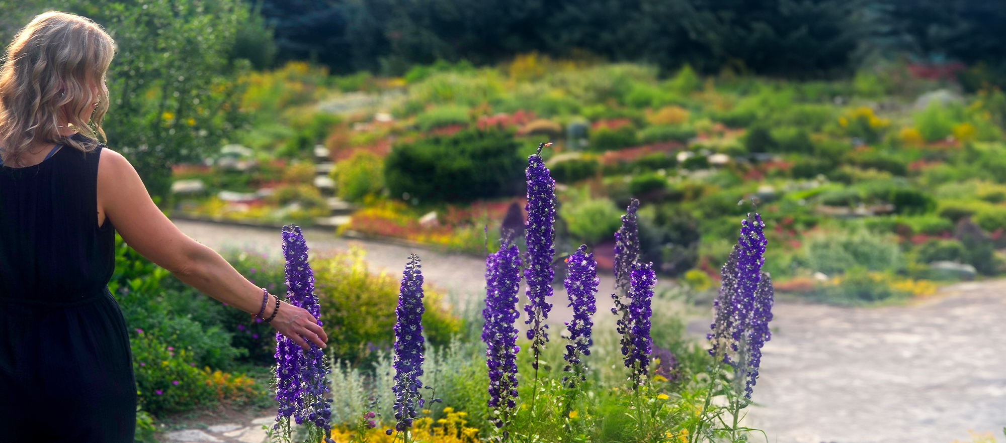 Photo of Inna Gunderson walking in a garden touching purple flowers