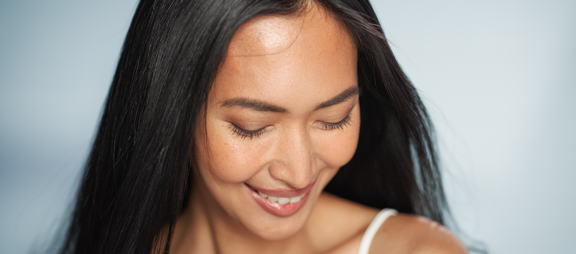 Asian woman with dark hair smiling gently on a light blue background